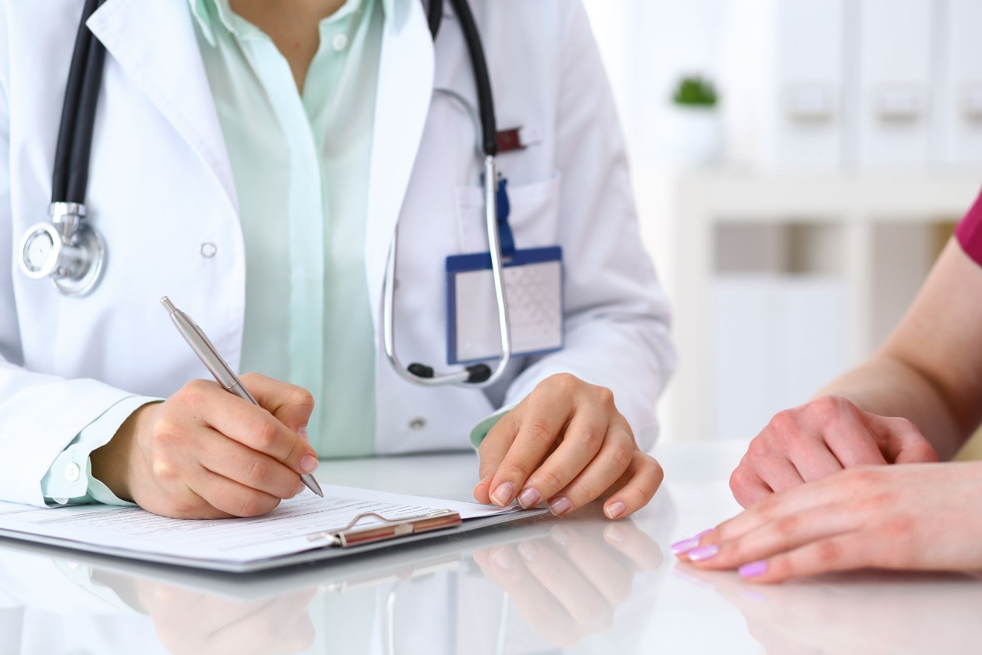 Doctor woman consulting patient while filling up an application form at the desk in hospital. Just hands close-up. Medicine and health care concept Doctor woman consulting patient while filling up an application form at the desk in hospital. Just hands close-up. Medicine and health care concept